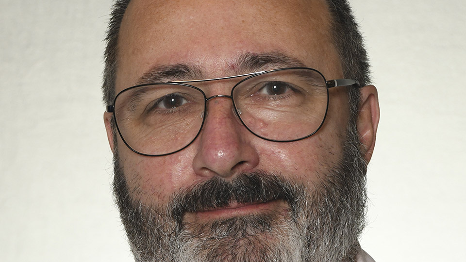 Person with short hair, glasses, and beard wearing a light pink shirt against a plain background